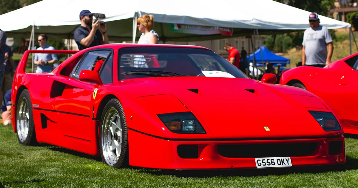 The legendary F40, still turning heads four decades later. Red supercar sitting parked on a grass show ground surrounded by onlookers.